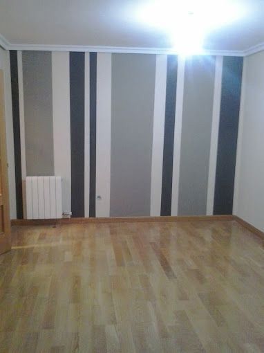 Habitación vacía con suelo de madera, papel pintado a rayas grises y una lámpara de techo brillante.
