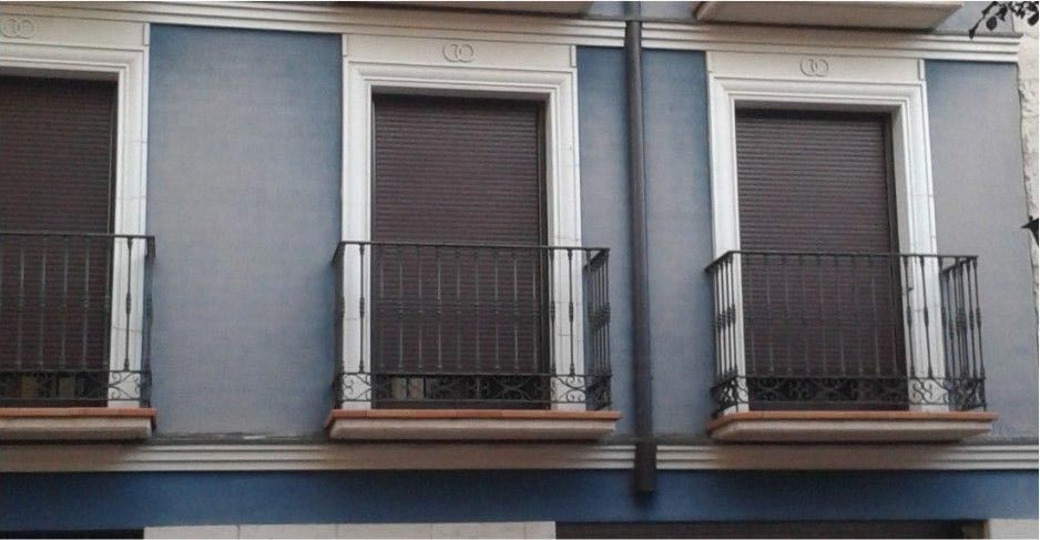 Hilera de balcones de apartamentos con contraventanas marrones cerradas y paredes de color azul grisáceo.